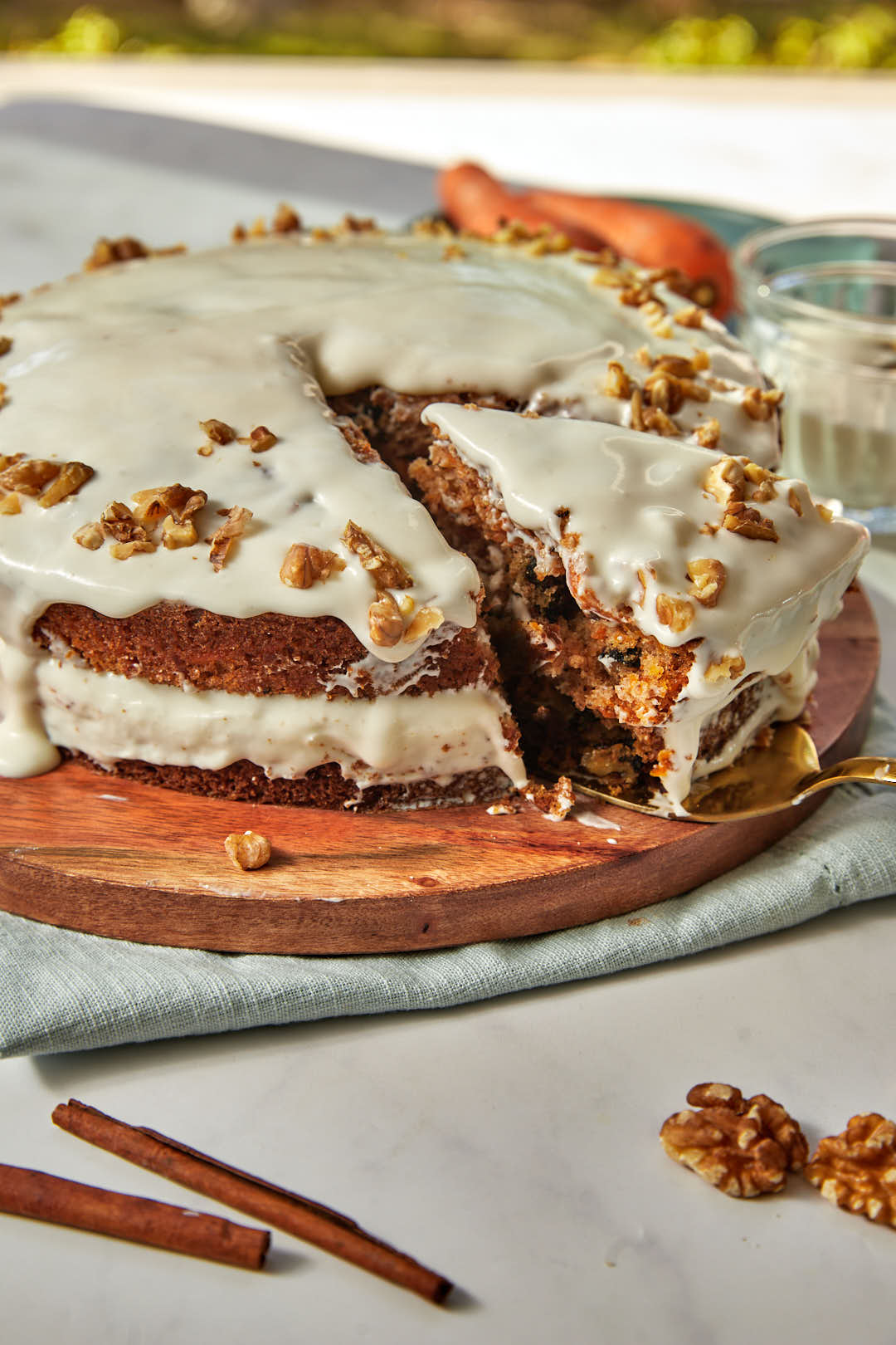 a whole carrot cake on a wooden cake plate with a slice being cut out.