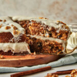 a slice of carrot cake being lifted off a wooden cake plate.