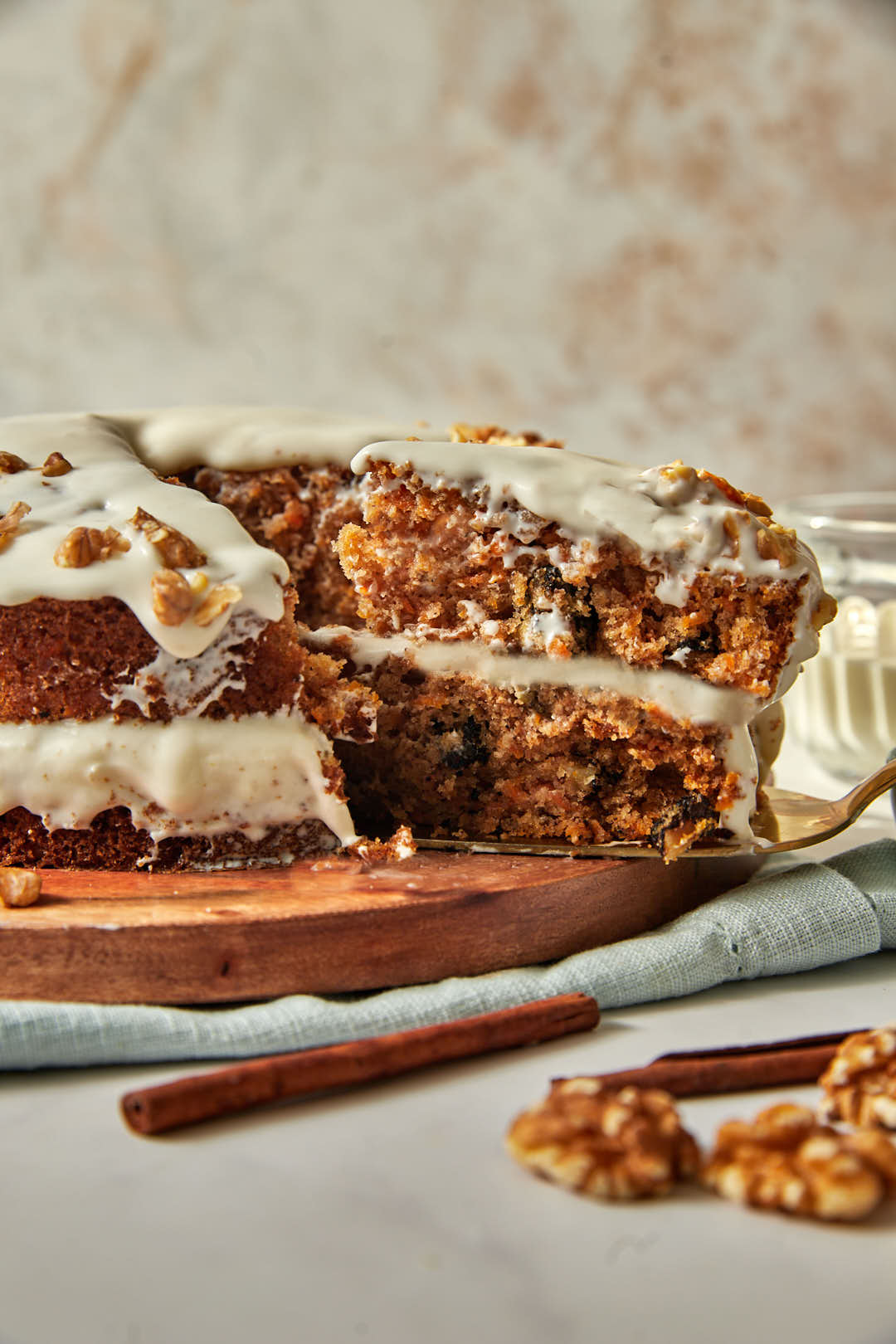 a slice of carrot cake being lifted off a wooden cake plate.