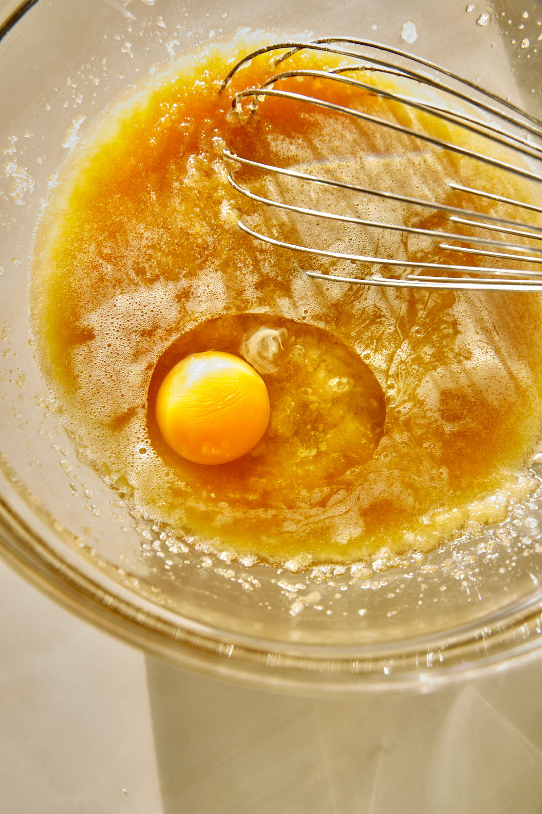 eggs being added to an olive oil sugar mix in a glass bowl.