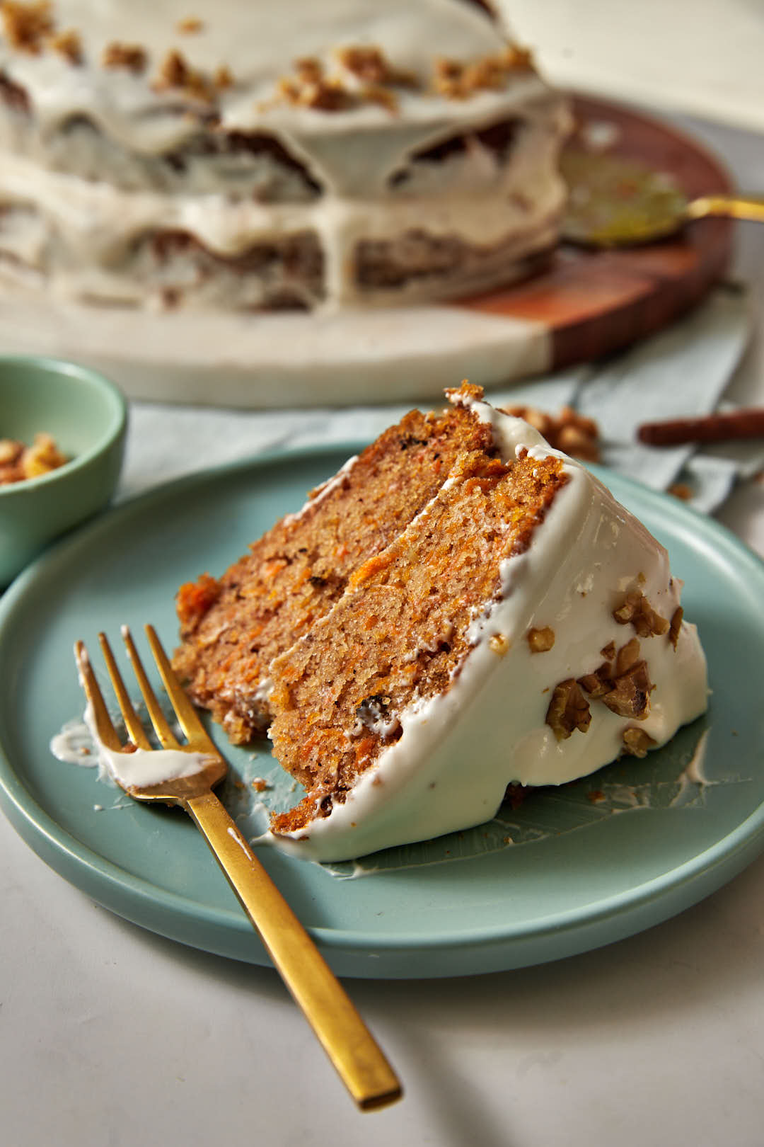 a slice of olive oil carrot cake on a blue plate with a gold fork.