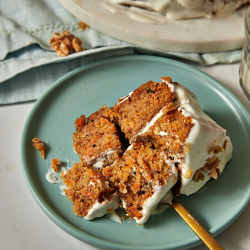 moist carrot cake on a blue plate with forkfuls being taken out.