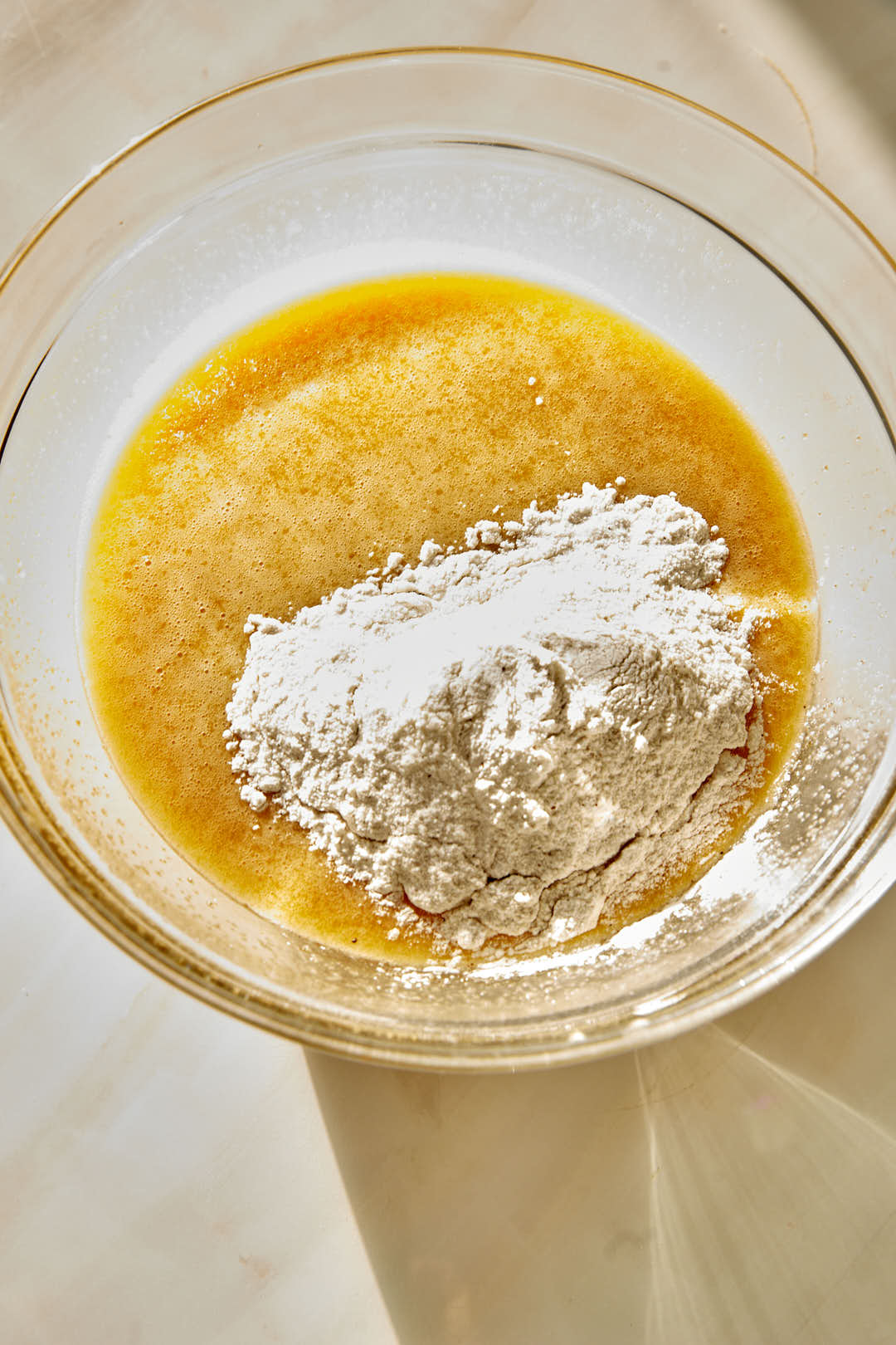 dry ingredients being added to wet ingredients for cake in a glass bowl.