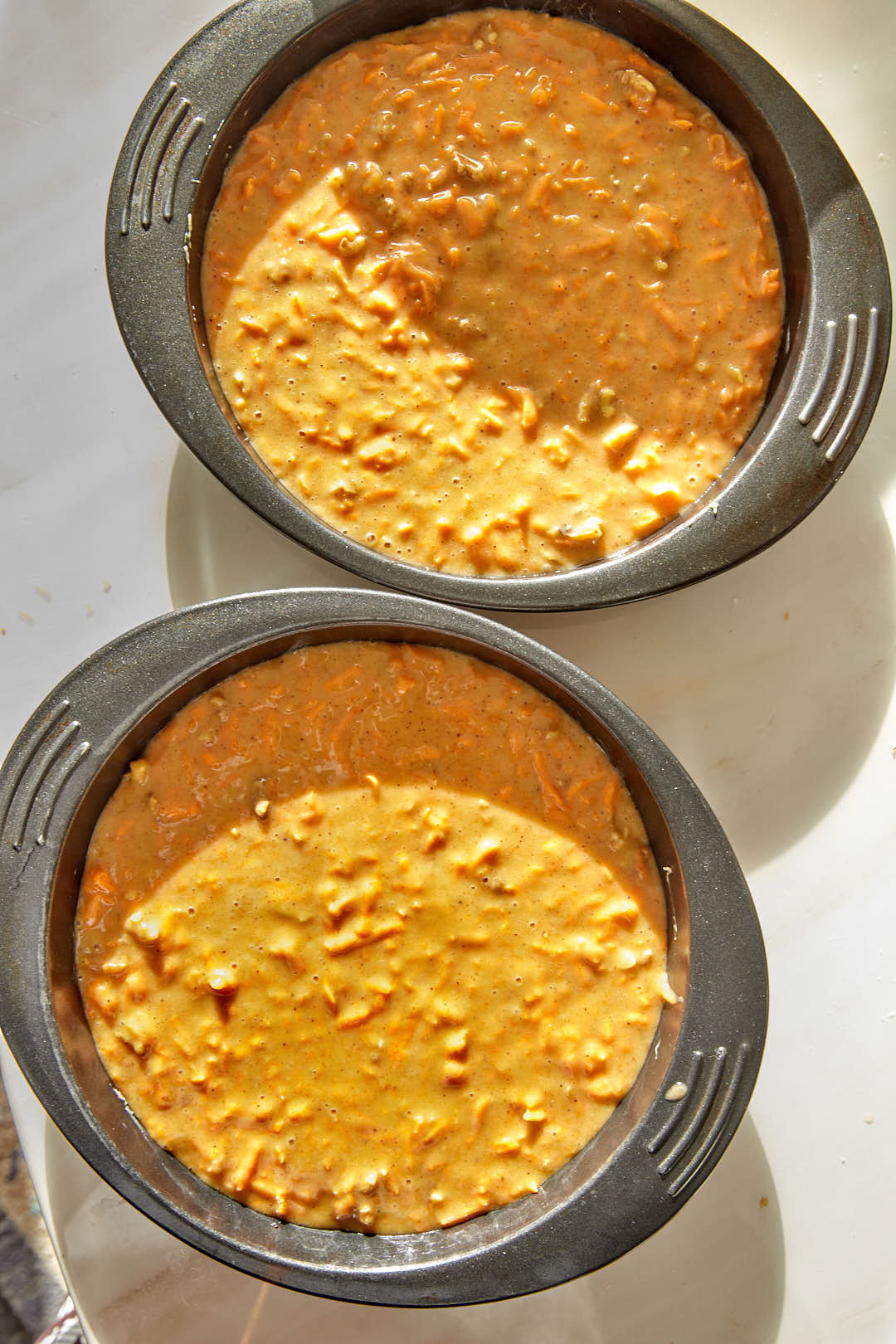 two 9 inch cake pans full of carrot cake batter on a white background .