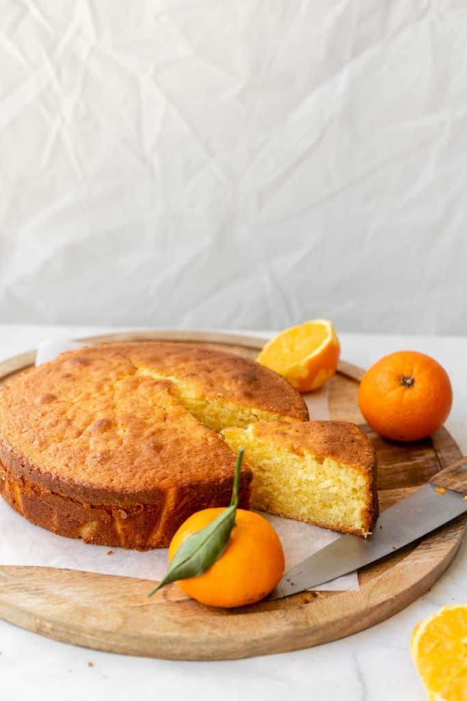 slice of orange cake on wooden platter with oranges in the background