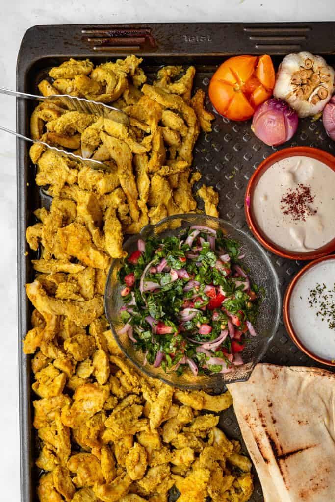 Baked chicken shawarma on a tray with assorted dips