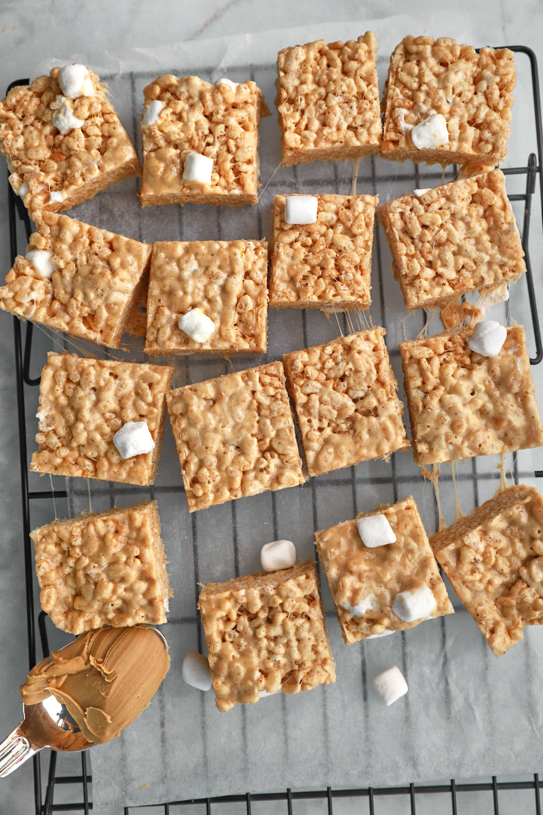peanut butter rice krispie squares topped with mini marshmallows on a wire rack, with a spoonful of peanut butter.