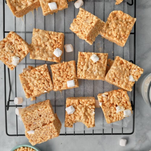 overhead view of peanut butter rice krispie squares on a wire rack with a bowl of Rice Krispies and a spoonful of peanut butter.