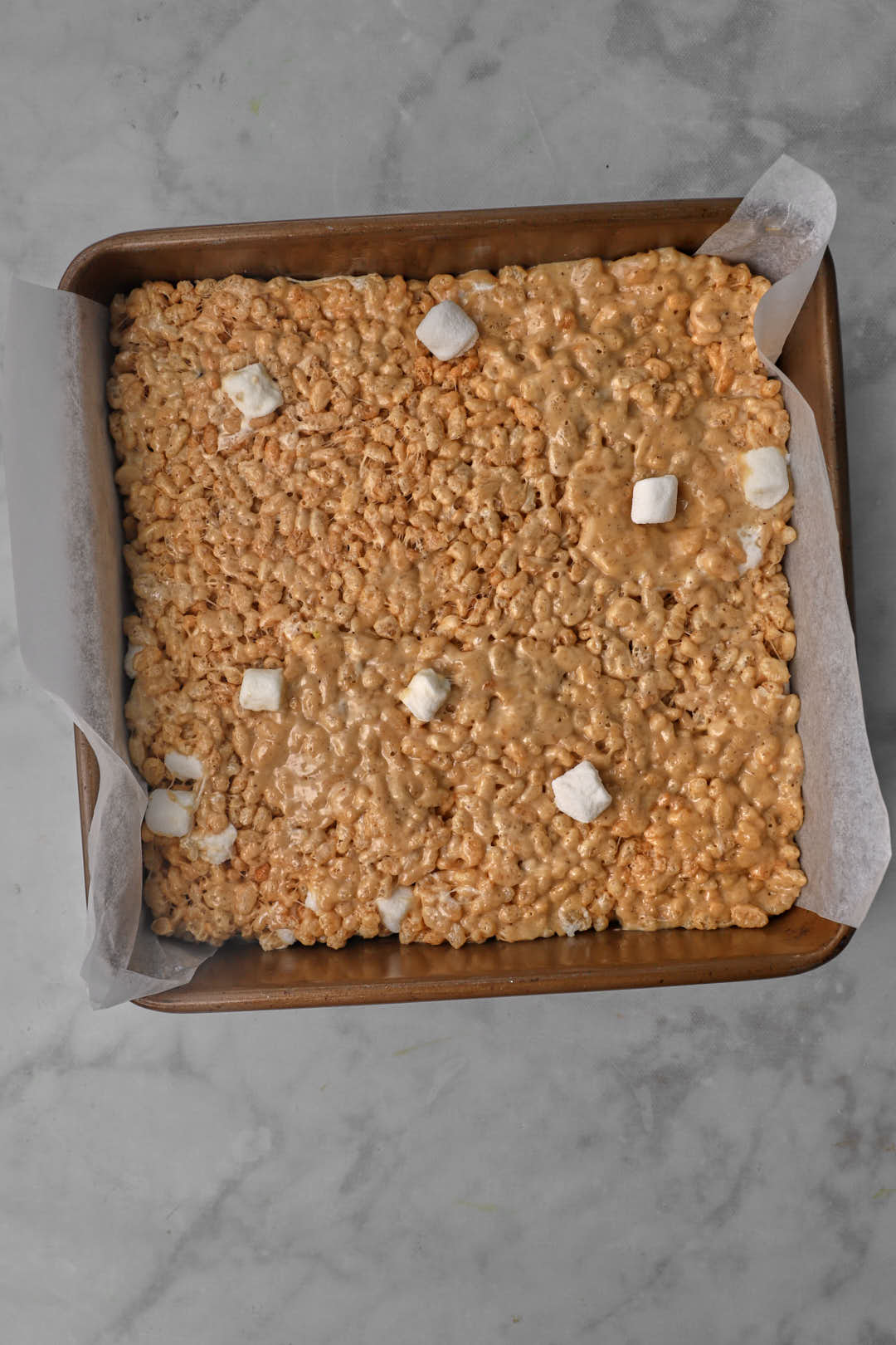peanut butter rice krispie mixture spread into a parchment-lined square baking pan.