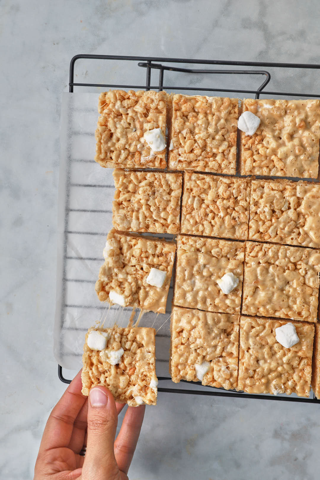 hand holding a peanut butter rice krispie square above more squares on a wire cooling rack.