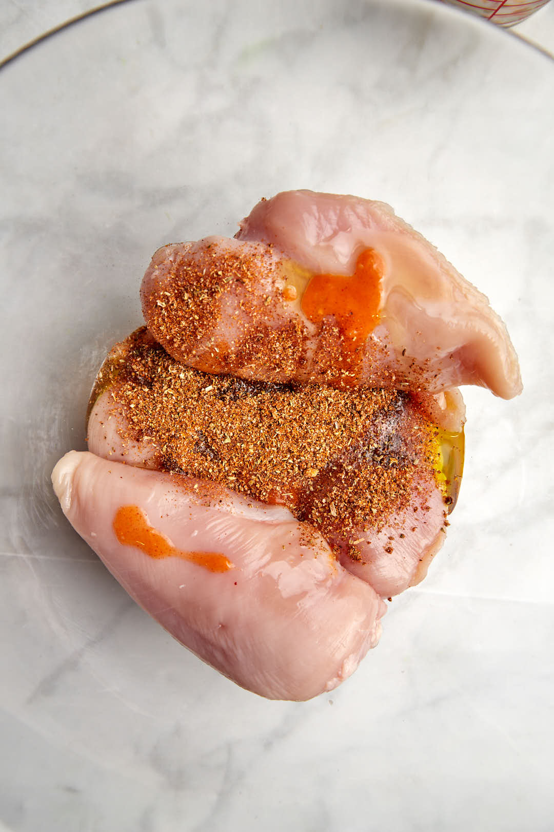 chicken breasts in a glass bowl with the spices and olive oil to marinade int he bowo.