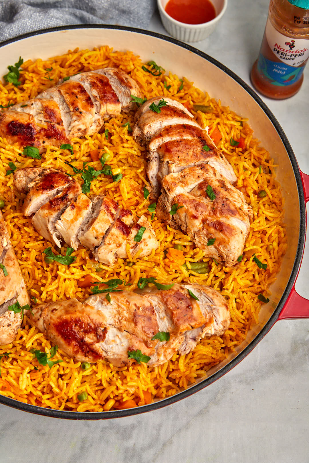 peri peri chicken and rice in a large skillet with peri peri sauce on the side.
