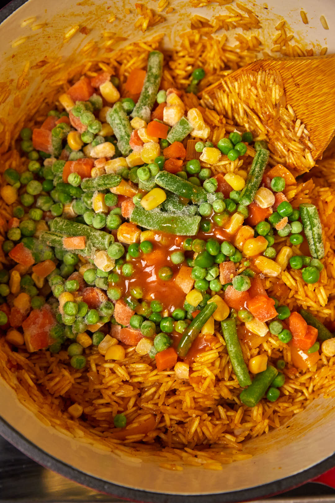 frozen peas, carrots, and corn added to basmati rice in a large skillet.