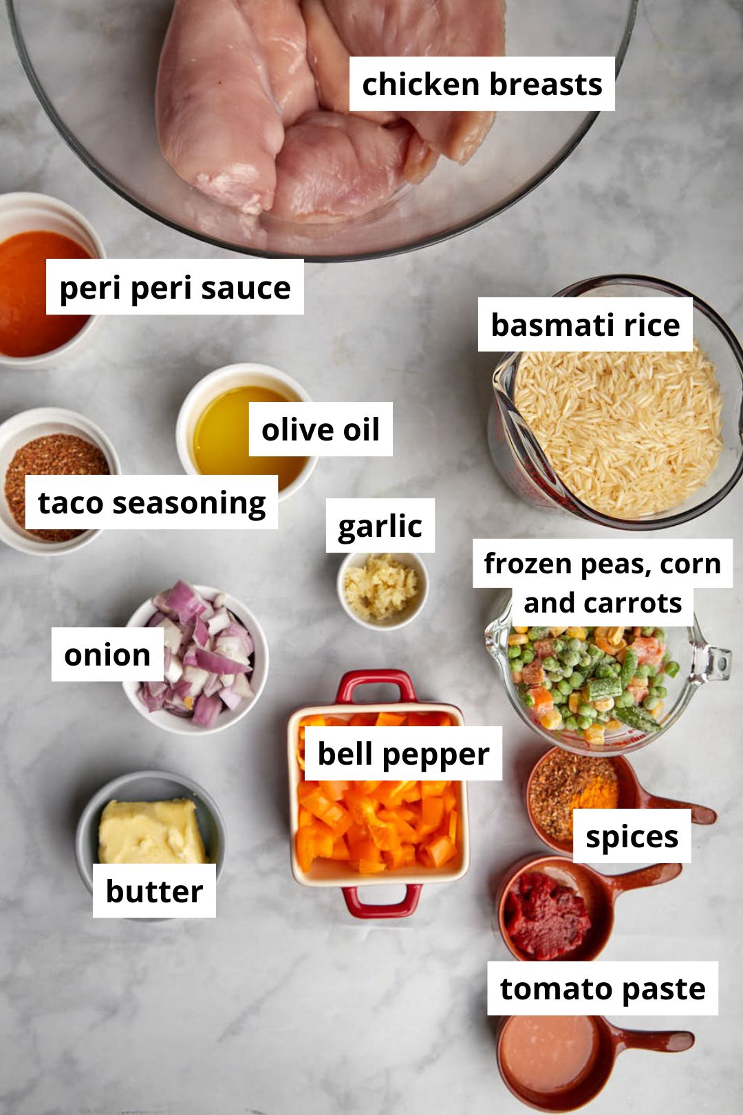 ingredients you need to make peri peri chicken an rice on a white marble background