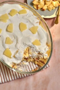 large pyrex dish of pineapple trifle on a pink background.