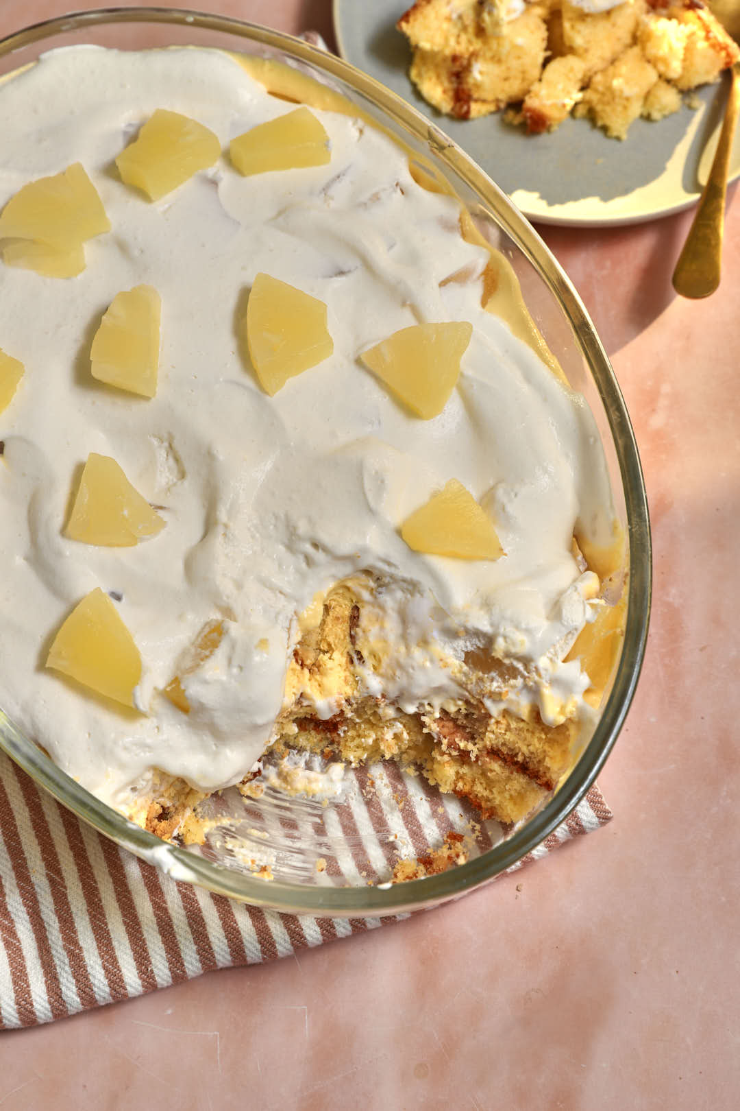 close up photo of pineapple trifle scooped out of a pyrex dish with a brown and white striped kitchen towel under it.