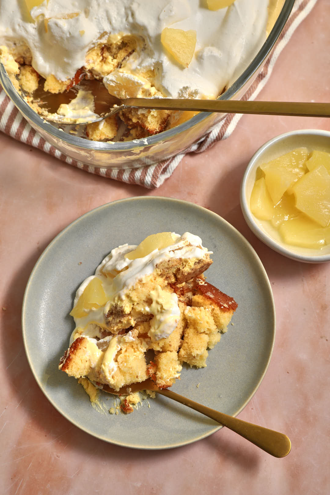 scoop of pineapple trifle on a gray plate with the larger portion of trifle in the background.