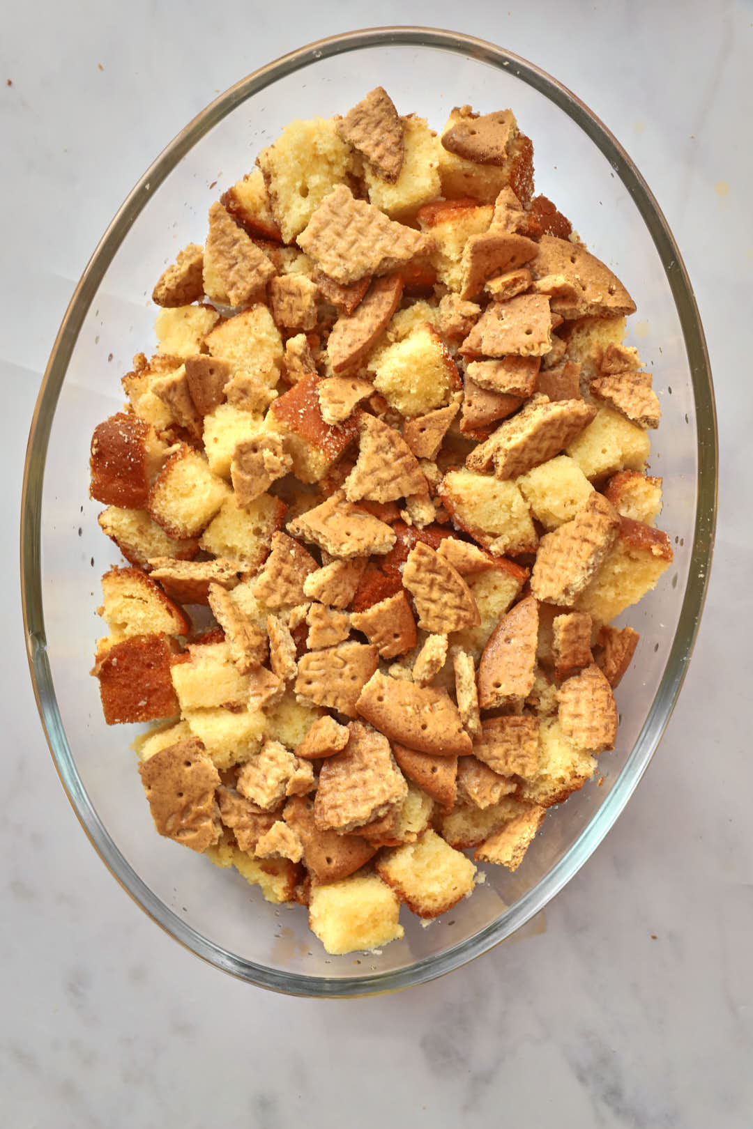 cubes of pound cake and biscuit chunks scattered on the base of a pyrex glass oval dish.