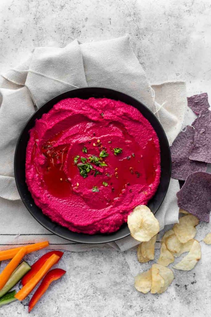 pink hummus in a bowl with chips and veggie sticks on the side