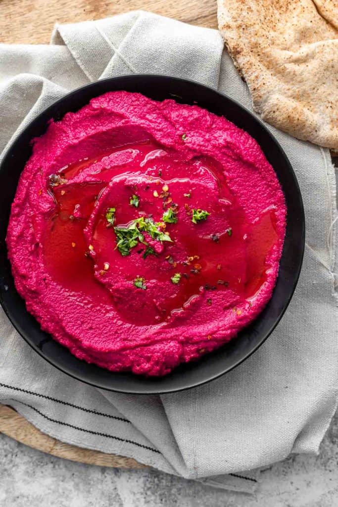 close up pic of beet hummus in black plate with pita bread on the side