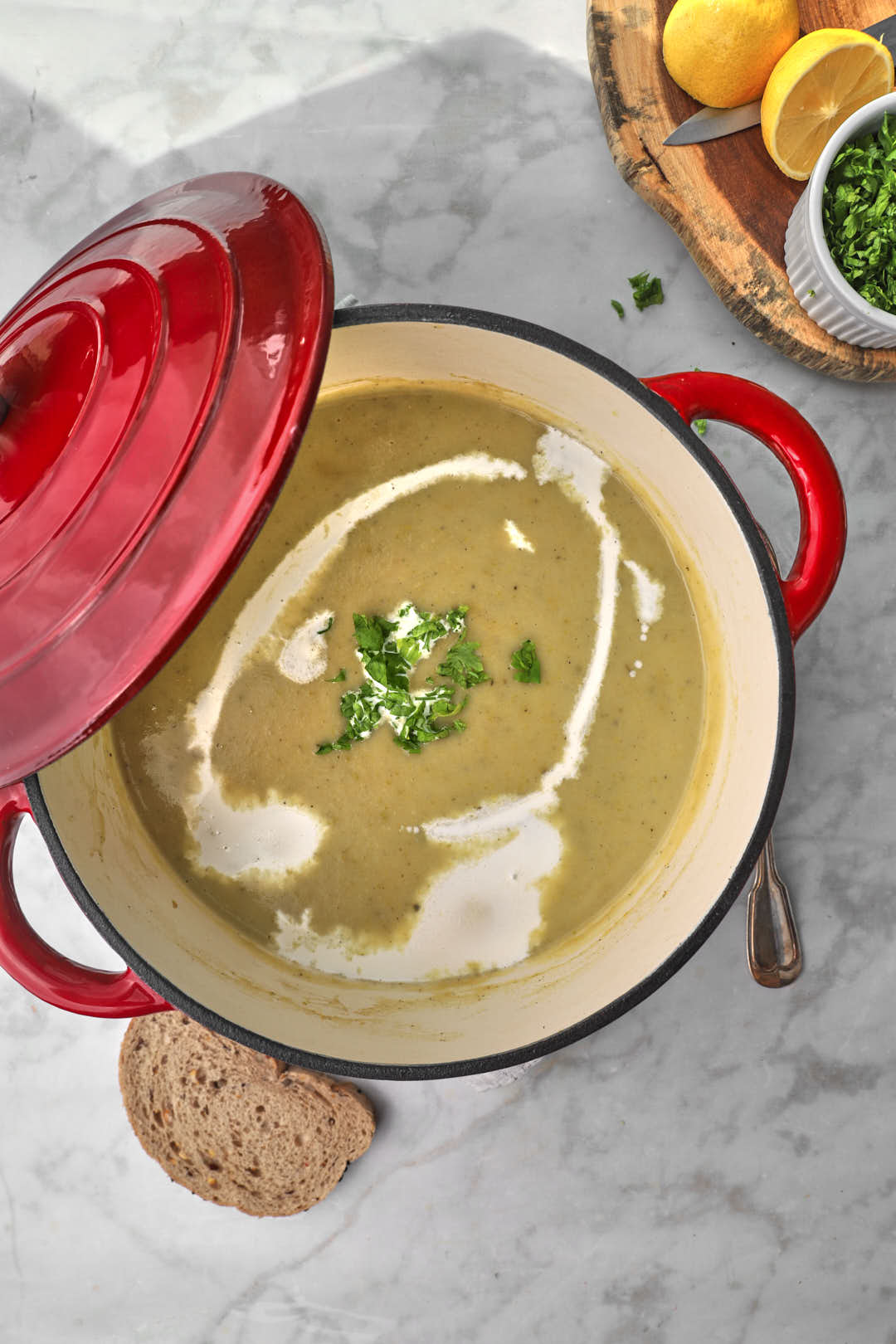 zucchini and potato soup in a red pot with a piece of bread on the background.