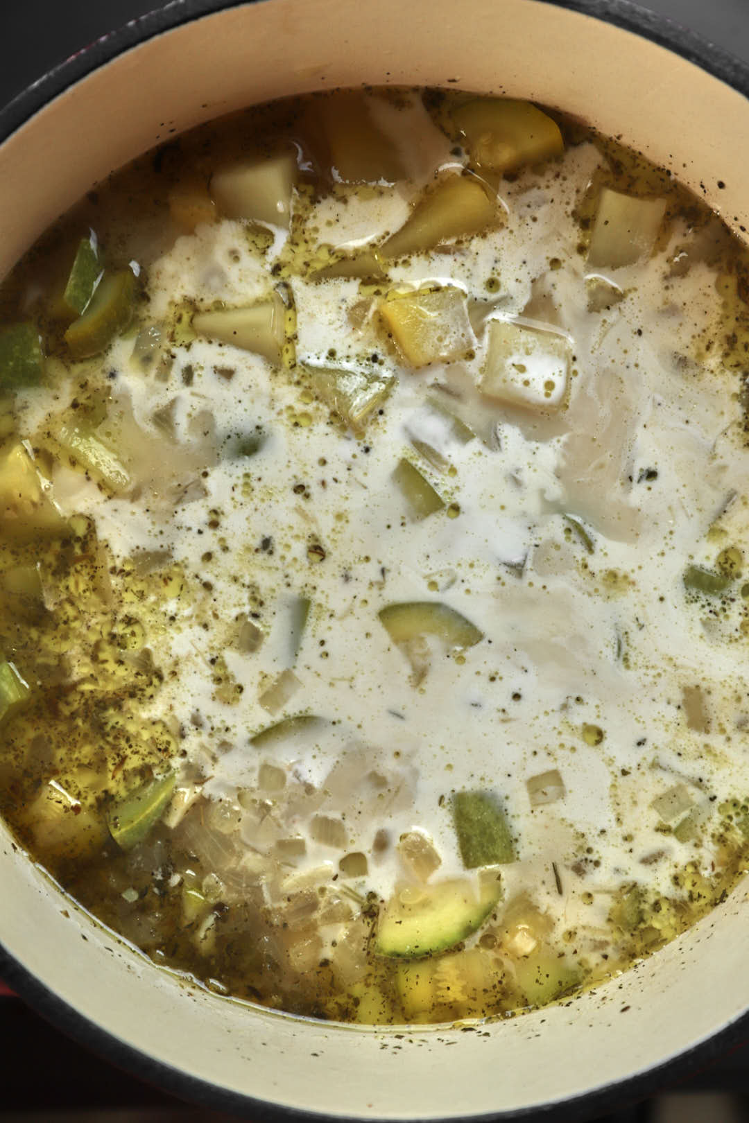 cream added to zucchini and potatoes and broth in a saucepan.