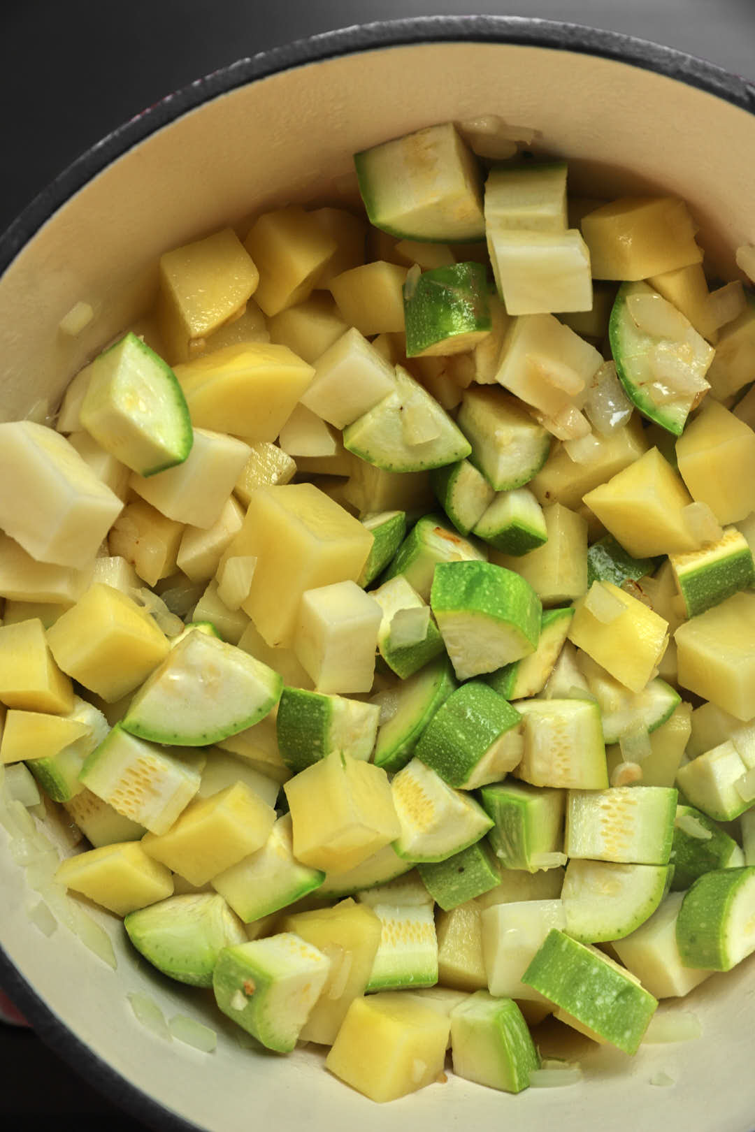 zucchini and potato cubes being sauteed in a soup pan.