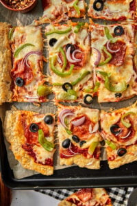 Close up photo of puff pastry pizza squares on a parchment lined baking sheet.