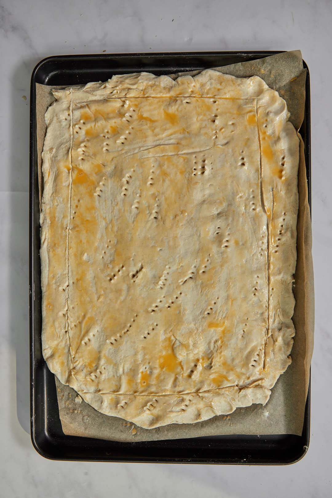 rectangle puff pastry on parchment paper lined baking sheet, spread with egg wash and pricked with a fork.