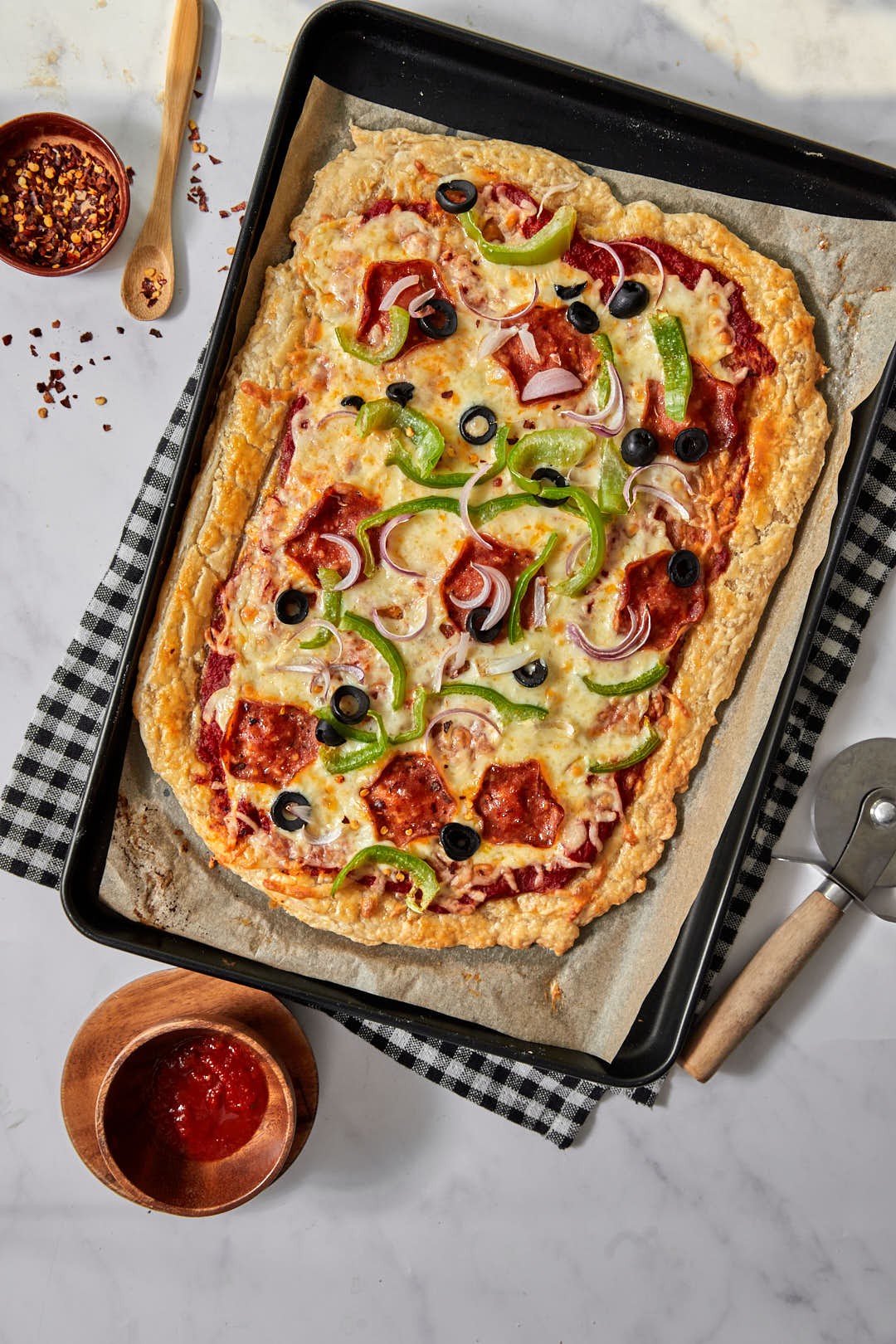 puff pastry pizza on a black and white checked towel with a pizza cutter on the side as well as red chili flakes.