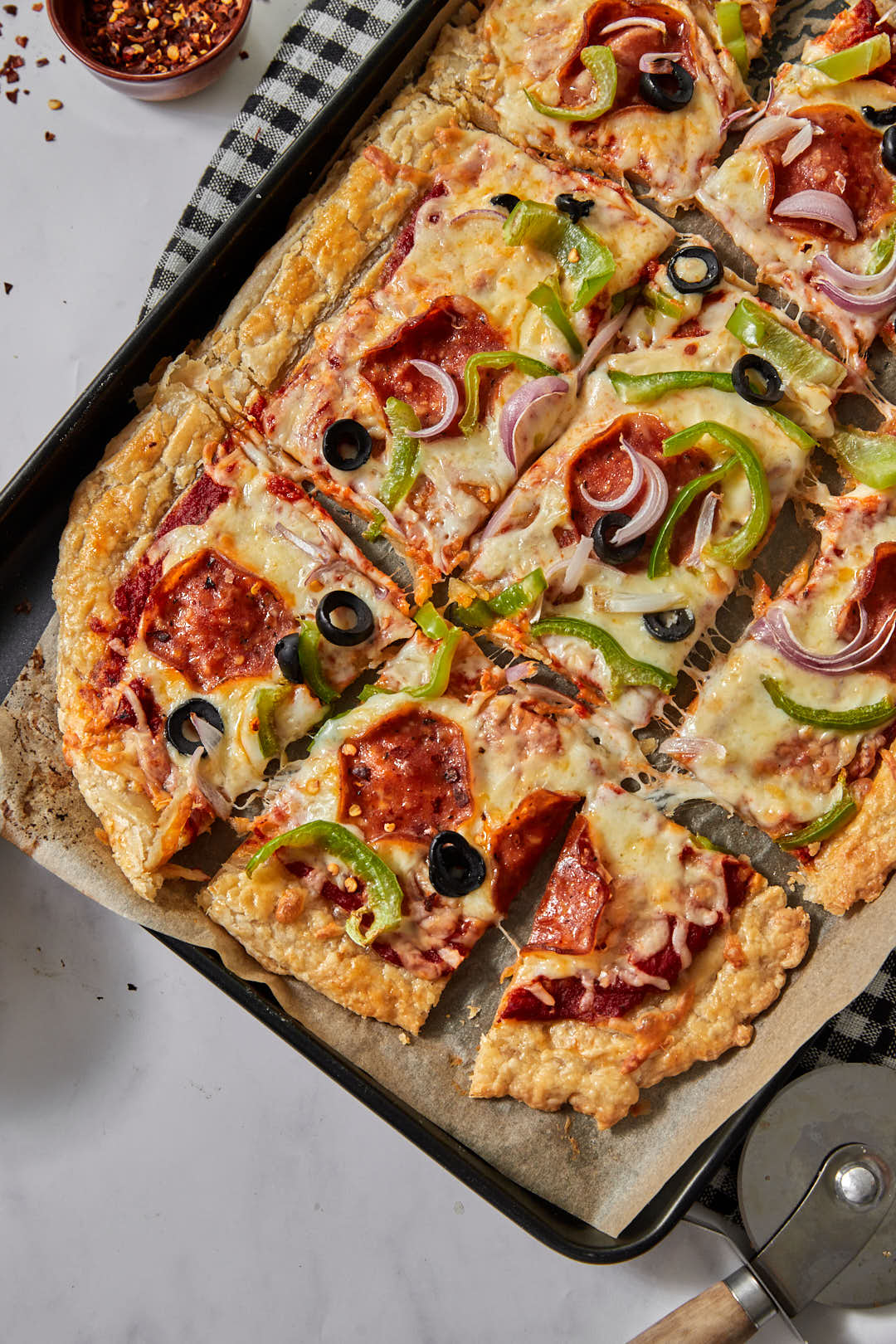 puff pastry pizza on a parchment paper lined baking sheet with pepperoni, olives, and green bell pepeprs, cut into squares.