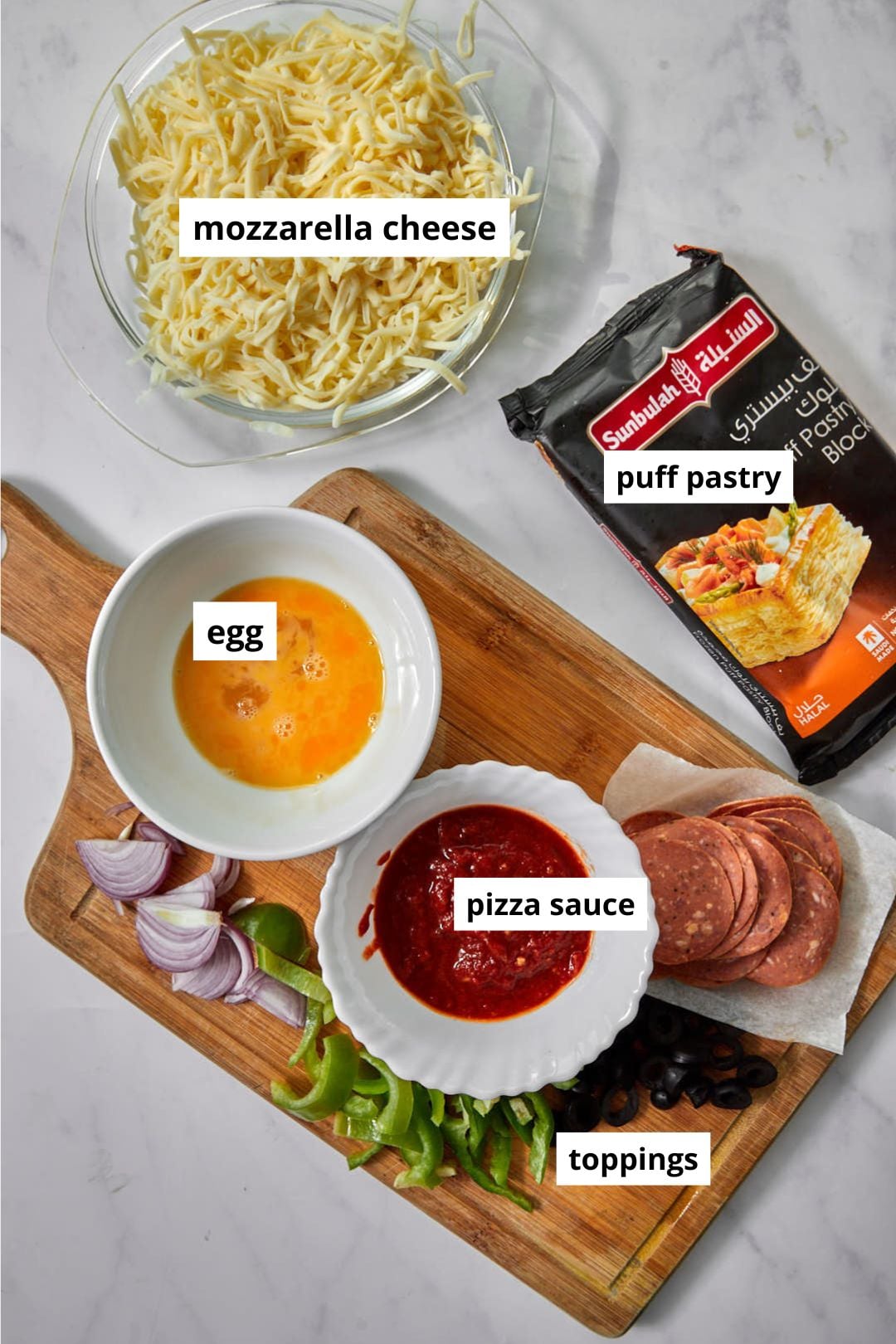 ingredients you need for puff pastry pizza on a white marble background.