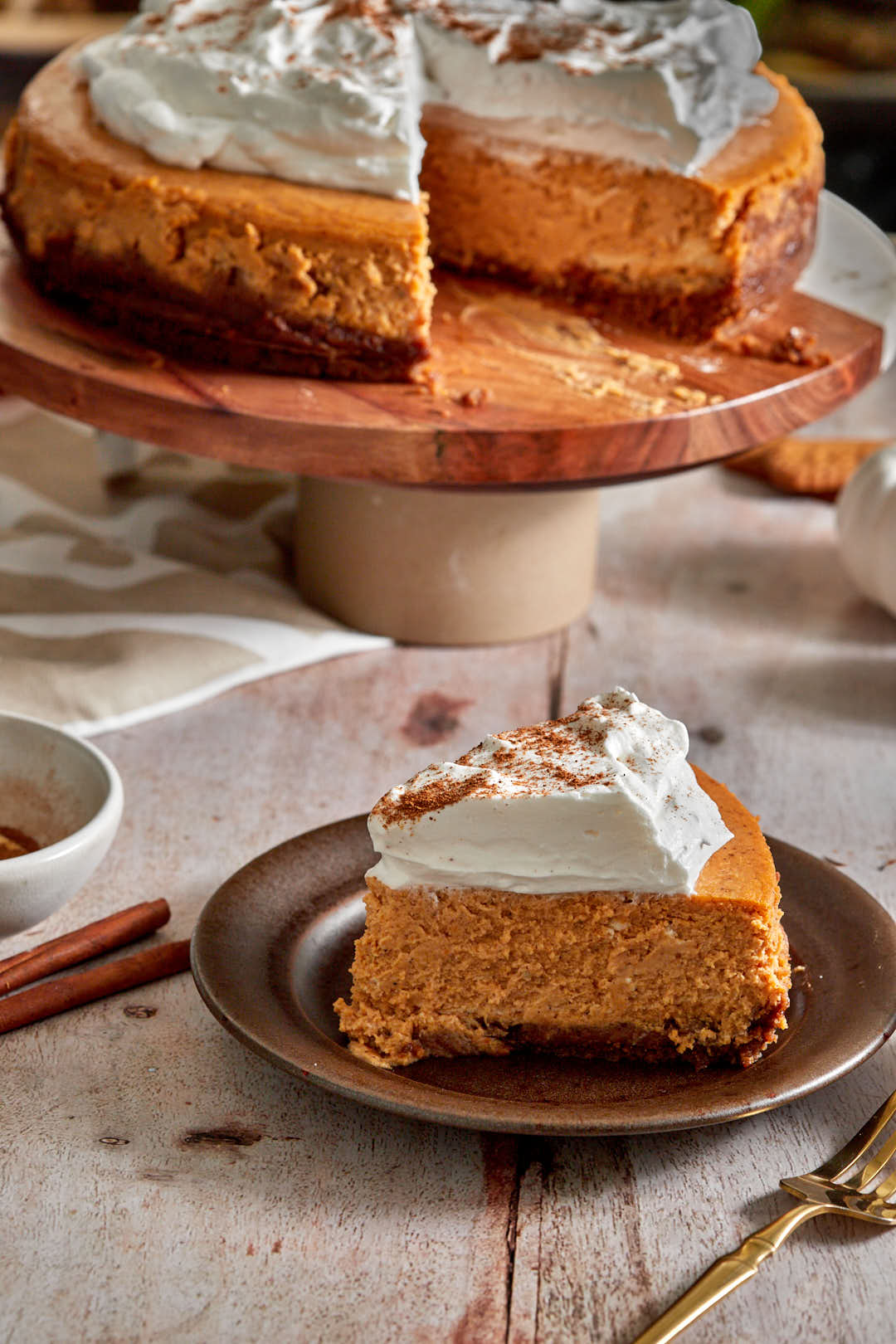 slice of pumpkin cheesecake on a small platew ith the remaining cheesecake on a cake stand in the background.