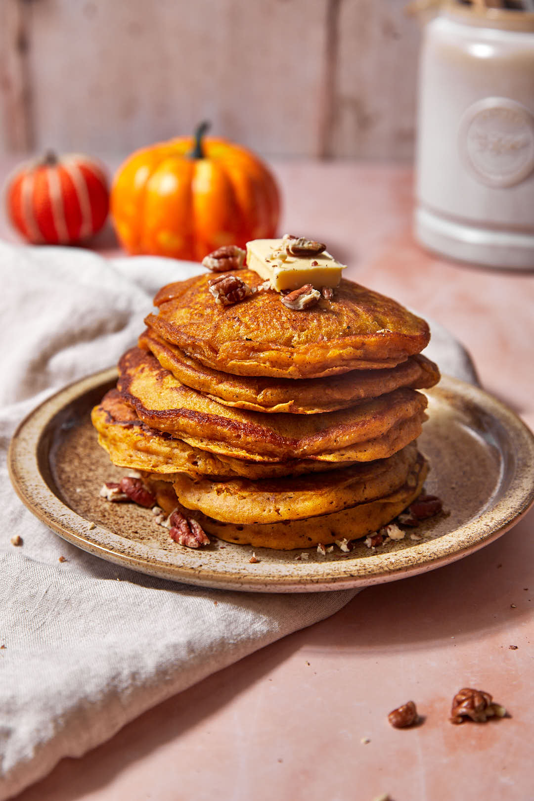 pumpkin pancakes on a beige plate with pumpkins in the background.