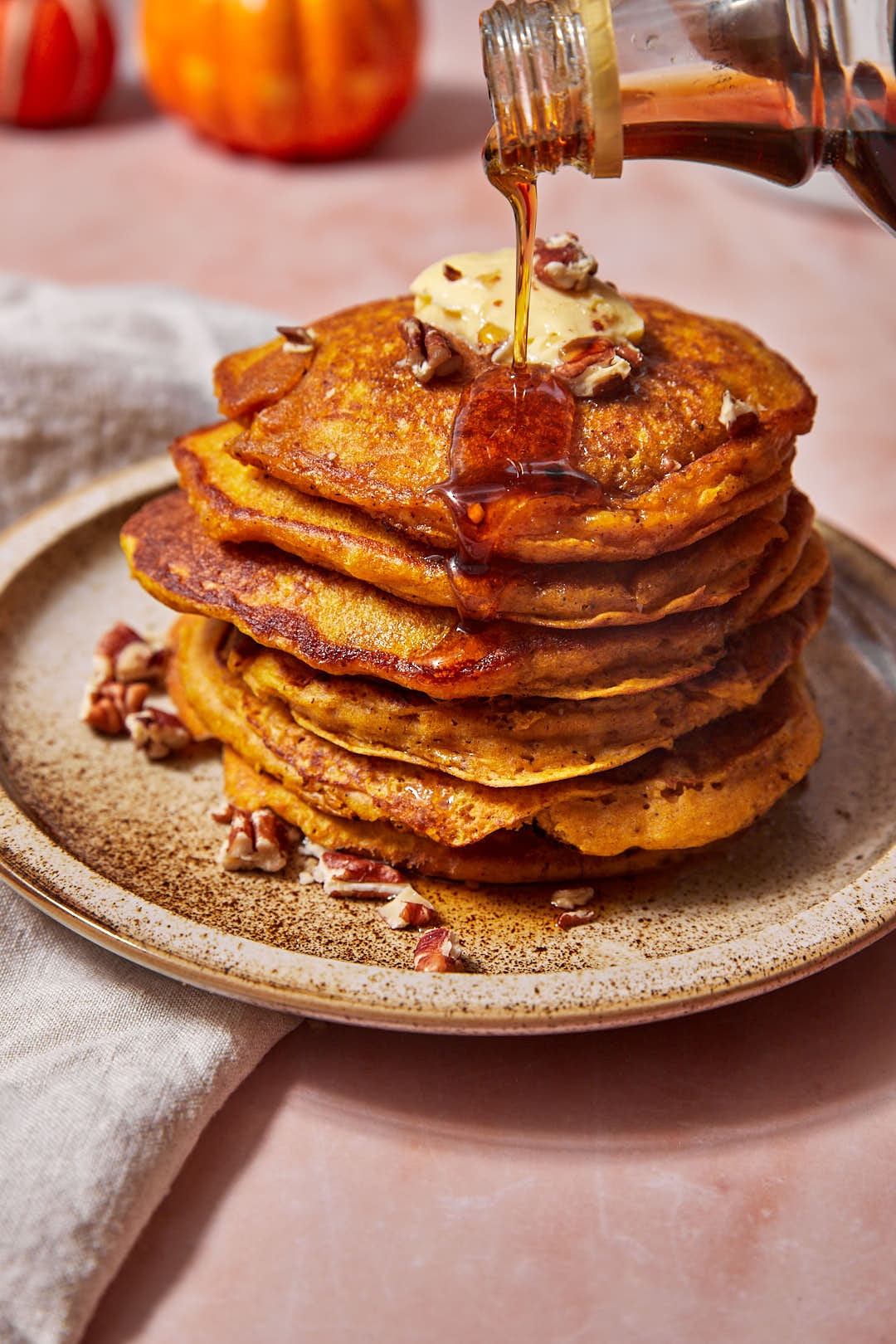 maple syrup being poured onto a stack of pumpkin pancakes on a plate.
