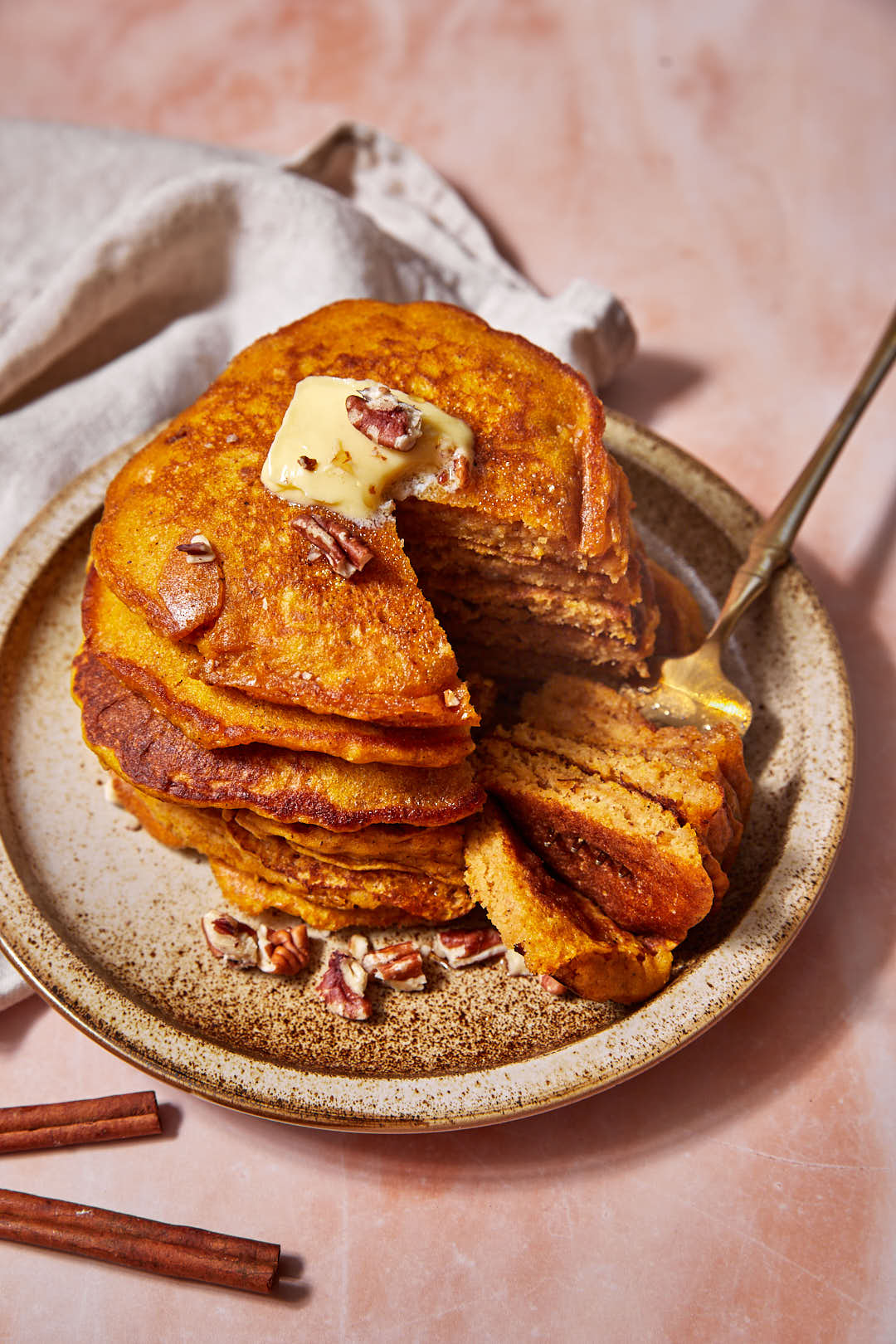 pumpkin pancake stacks with a fork in them on a beige plate.