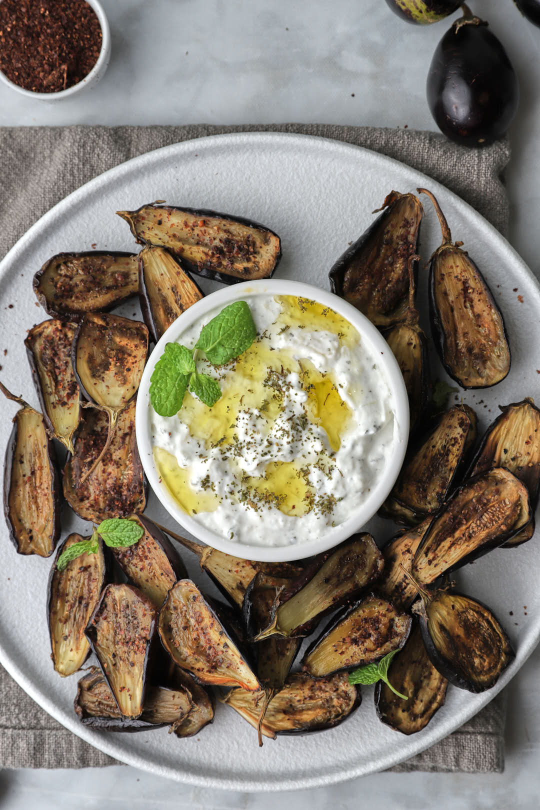 roasted baby eggplant on a plate with garlic yogurt sauce in the center.
