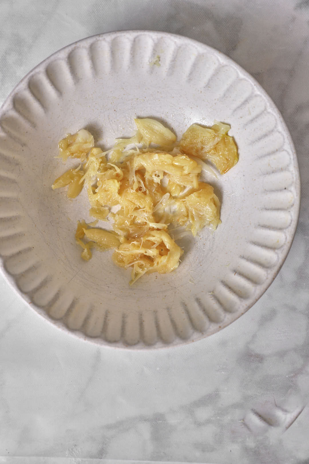 Roasted garlic cloves squeezed out into beige bowl.