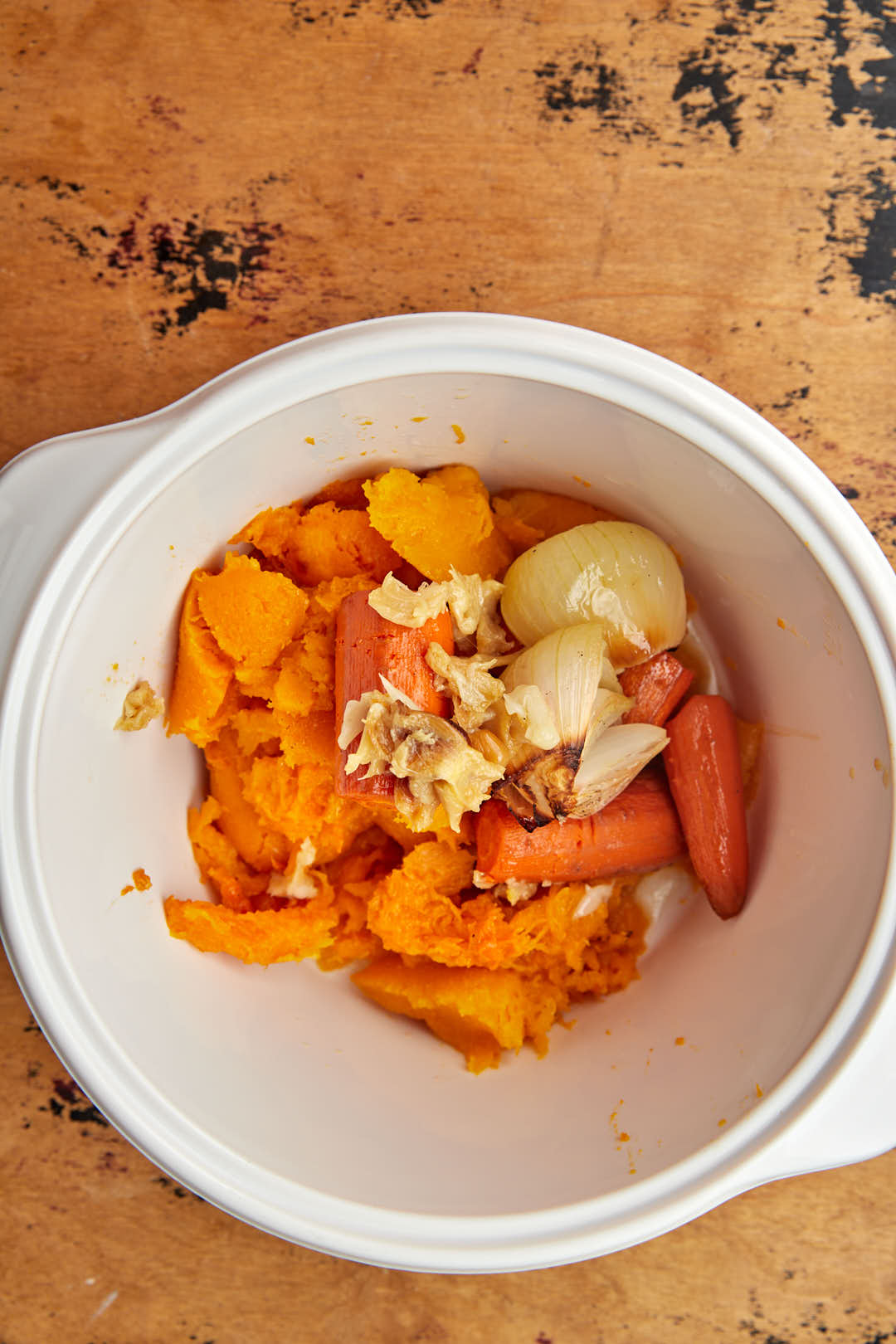 roasted butternut squash, carrots, onions and garlic scooped out into a white saucepan.