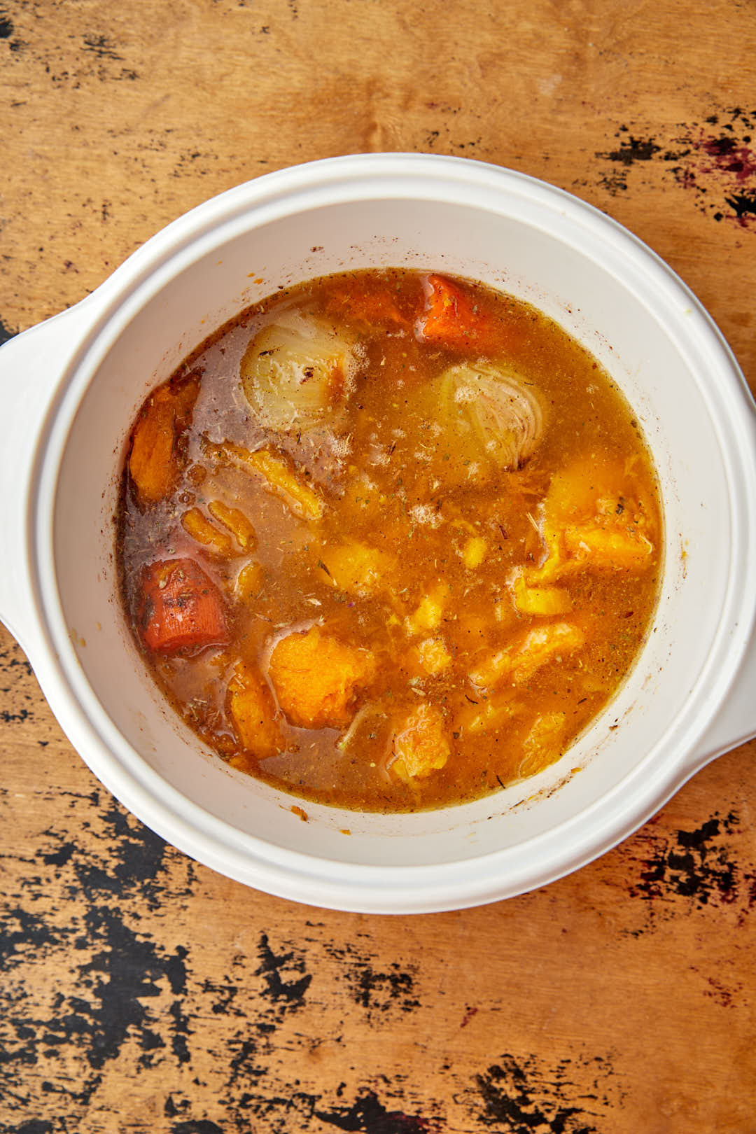simmering vegetable stock with vegetables in a white saucepan.