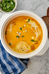 a white pot with butternut squash soup in it on a blue kitchen towel with green onions in the background