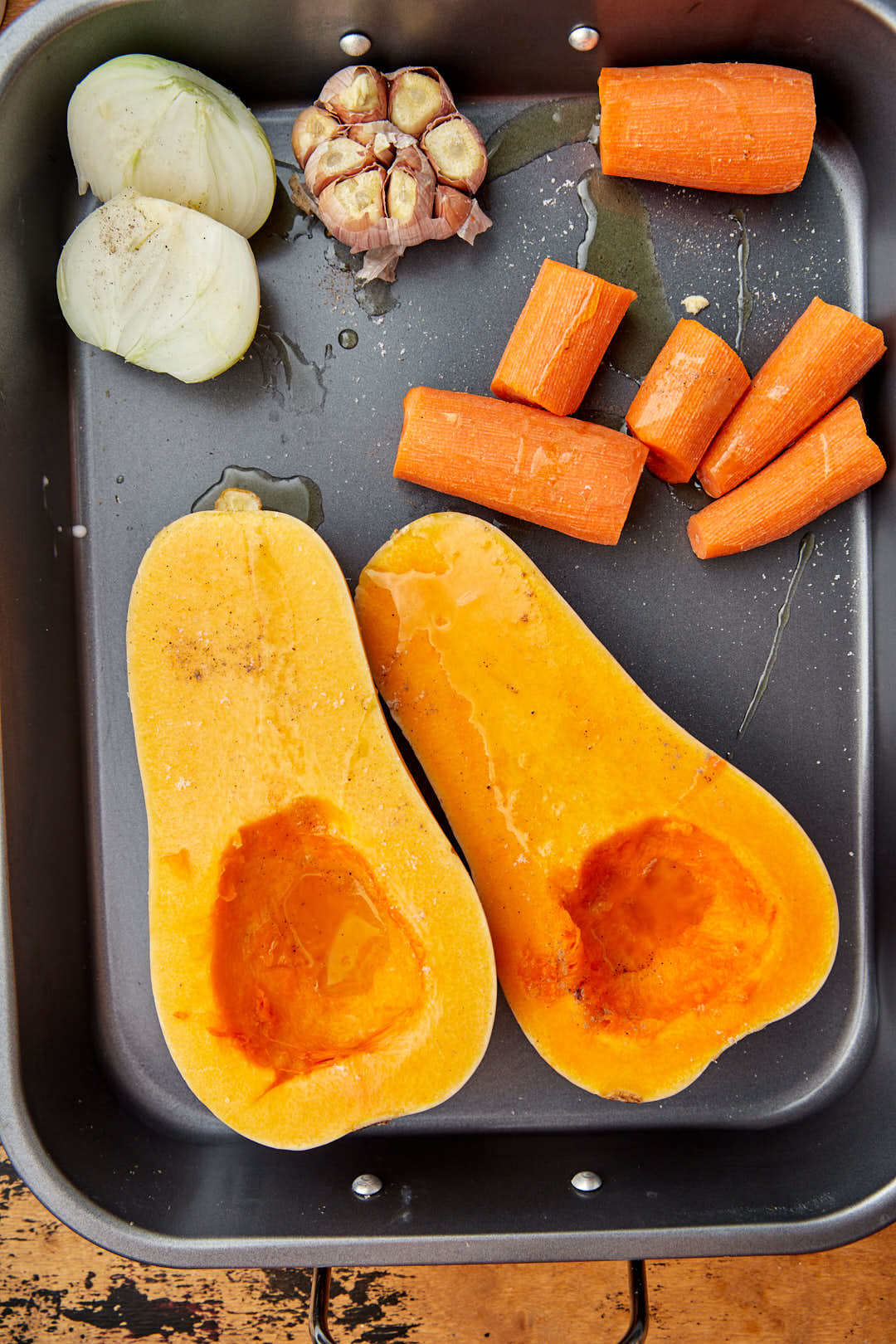 halved butternut squash and chopped carrots and onion on a roasting tray