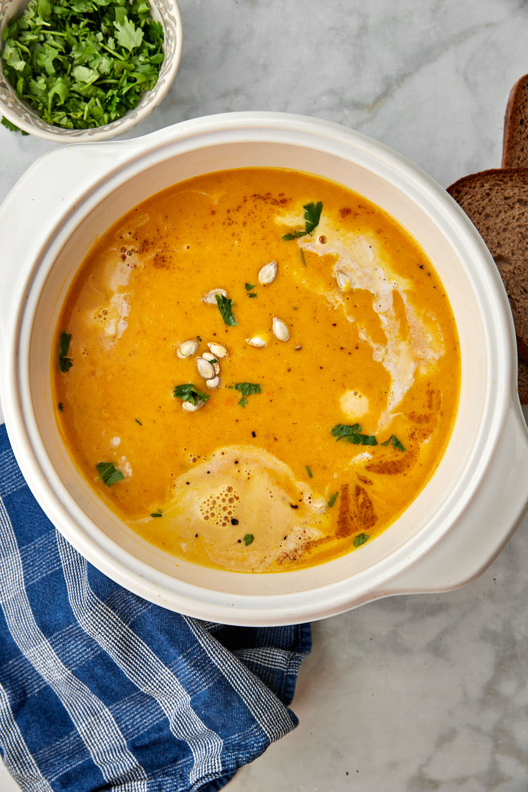 a white pot with butternut squash soup in it on a blue kitchen towel with green onions in the background