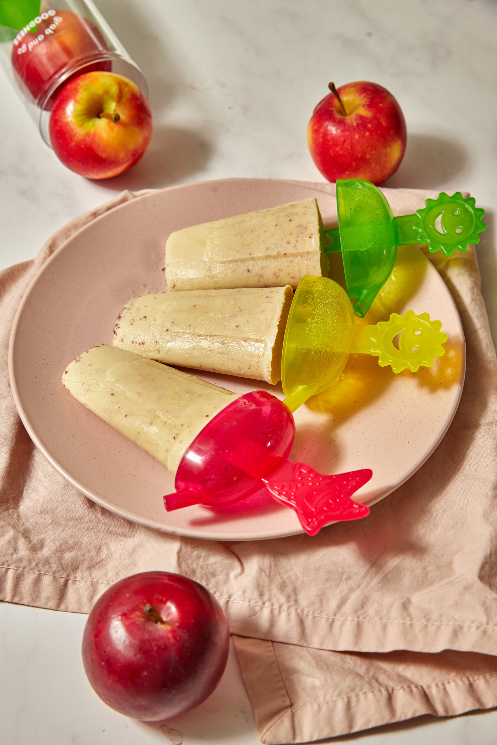 apple yogurt popsicles on a pink plate with more apples in the background.