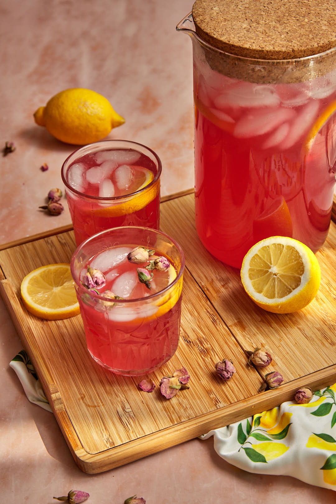 two glasses filled with rose lemonade with a pitcher of lemonade in the background.