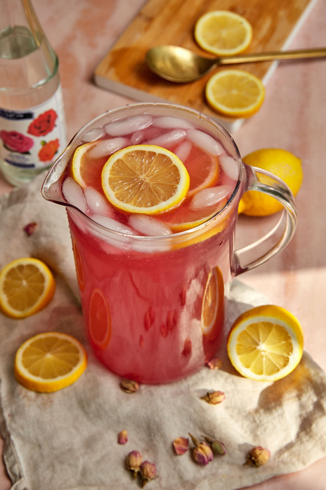 Rose lemonade in a glass pitcher with slices of lemons in the pitcher and around.
