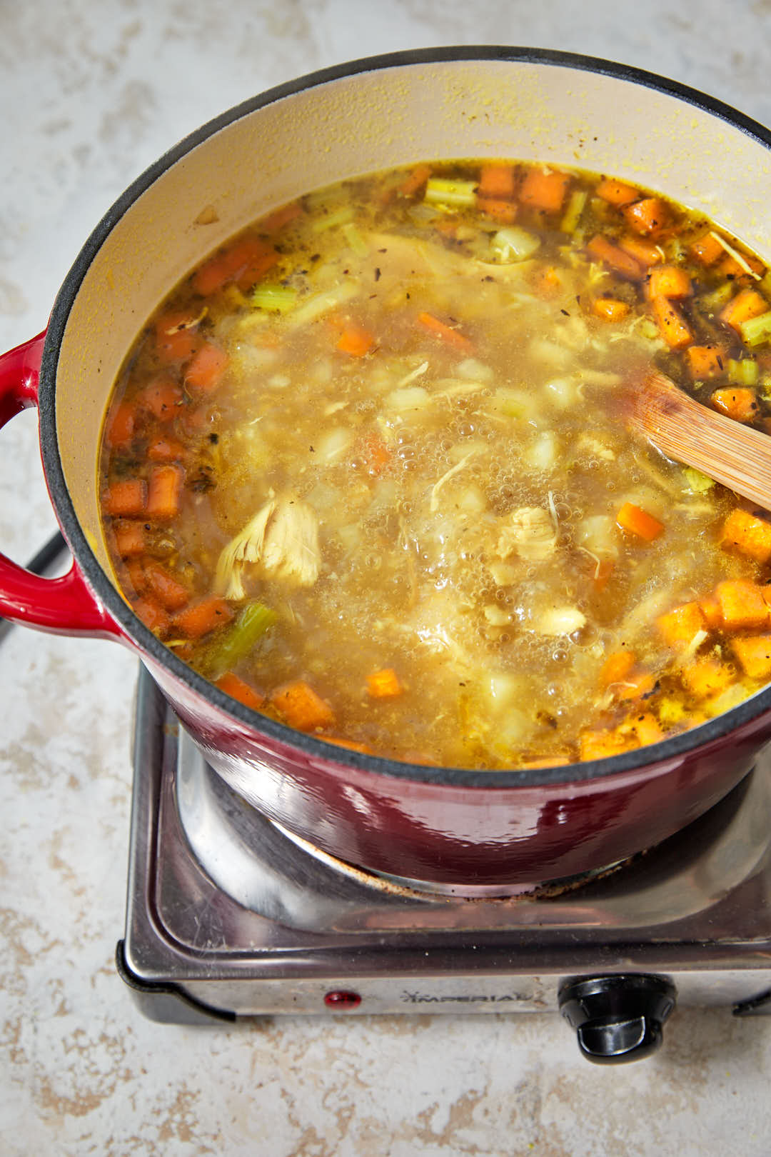 shredded rotisserie chicken added to the soup broth in a pot.