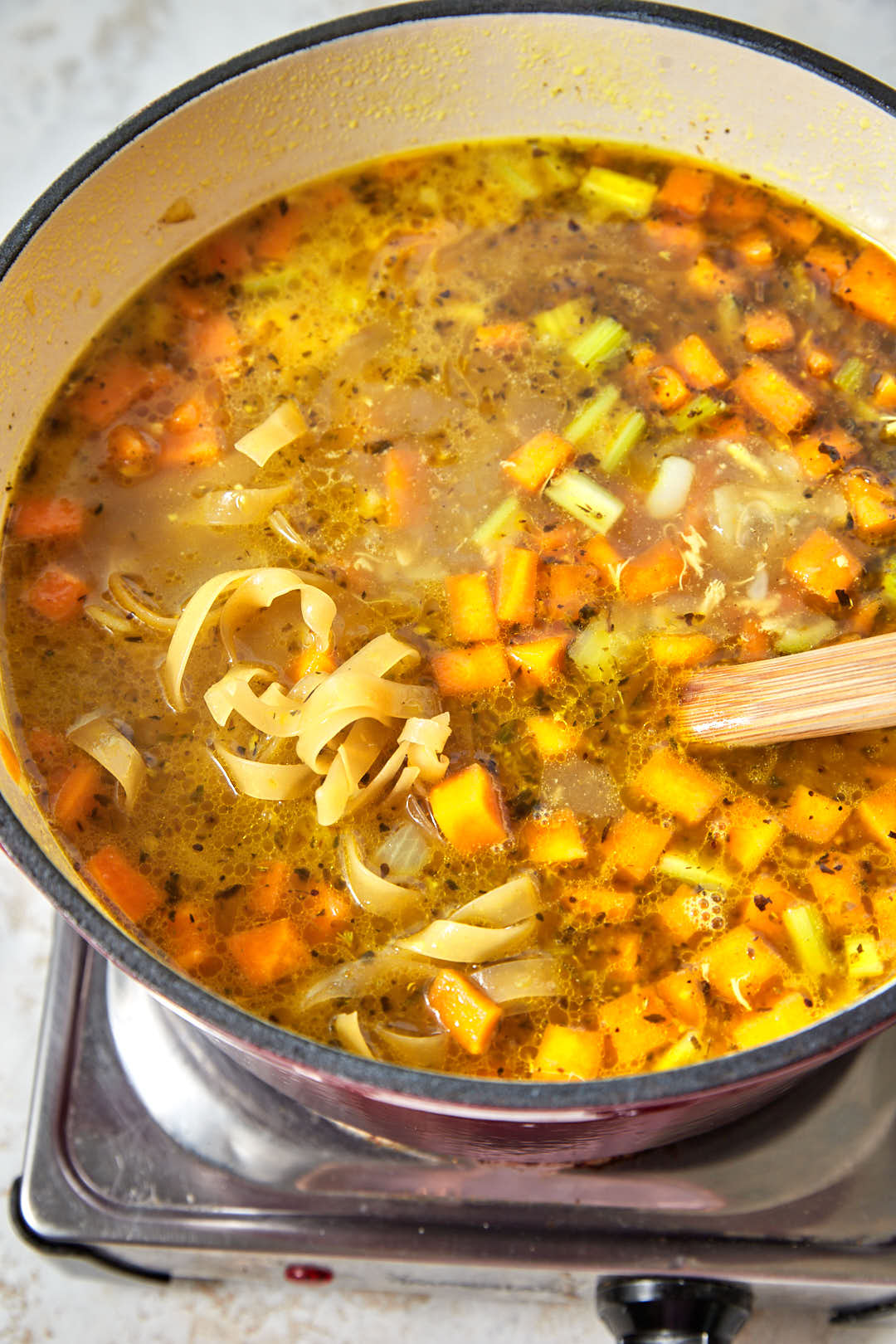 tagliatelle noodles added to chicken soup in a pot.
