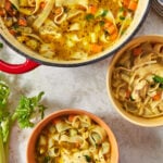 two bowls of rotisserie chicken noodle soup next to a red pot of soup.