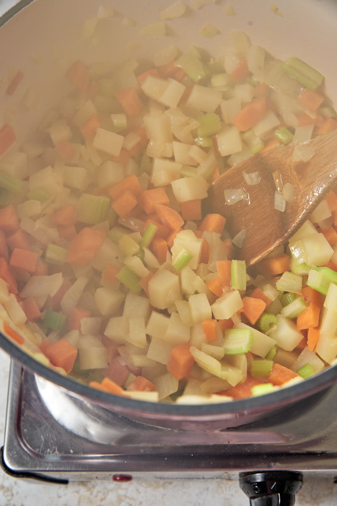 softened diced vegetables cooking in a pot with a wooden spoon.